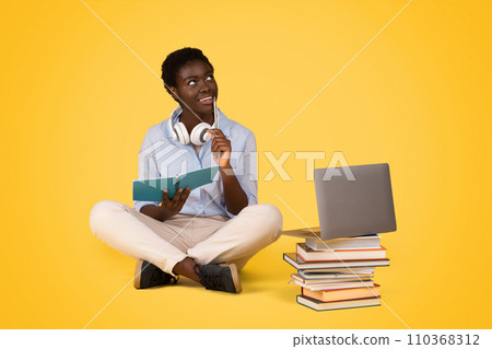 Smiling pensive teen black lady student sit with laptop on floor Smiling pensive teen black lady student sit with laptop on floor 110368312