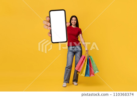Happy asian woman posing with purchases and showing cellphone 110368374