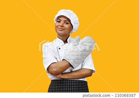 Confident black female chef with crossed arms wearing an oven mitt Confident black female chef with crossed arms wearing an oven mitt 110368387