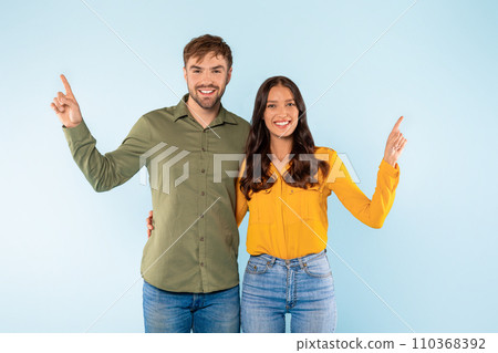 Smiling couple pointing upwards on light blue background 110368392