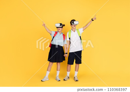 Two schoolchildren with backpacks are engaged in a virtual reality experience, pointing upwards Two schoolchildren with backpacks are engaged in a virtual reality experience, pointing upwards 110368397
