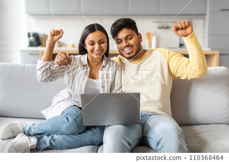 Portrait Of Joyful Young Indian Couple Celebrating Success With Laptop At Home 110368464