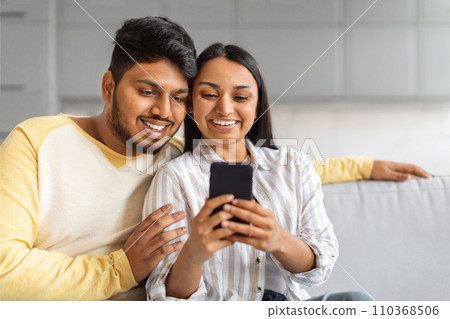 Portrait Of Happy Indian Couple Resting With Smartphone On Couch Portrait Of Happy Indian Couple Resting With Smartphone On Couch 110368506