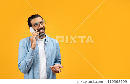 A man with a beard and glasses cheerfully talks on the phone, gesturing with his free hand A man with a beard and glasses cheerfully talks on the phone, gesturing with his free hand 110368509