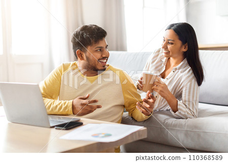 Cheerful Indian Couple Relaxing With Laptop And Coffee In Living Room 110368589
