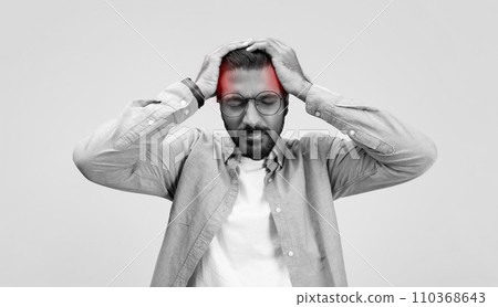 A stressed man in a casual linen shirt and glasses grasps his head in frustration or headache 110368643