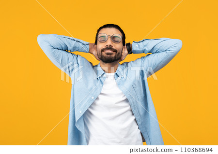 Relaxed man in a blue denim shirt, hands behind head, eyes closed, smiling peacefully 110368694