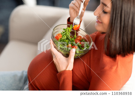 Pregnant lady eating vegetable salad resting on sofa at home 110368938