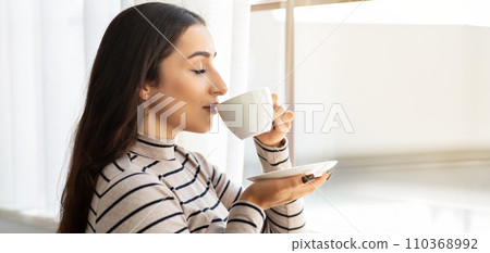 A serene young woman with long dark hair, wearing a striped turtleneck, enjoys a moment 110368992