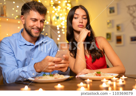 Smiling man on phone, woman disenchanted at dinner 110369079