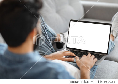 Indian Man Using Laptop Computer With Blank White Screen At Home 110369084