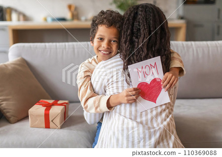 Black Boy Holding Handmade Greeting Card With Red Heart And Embracing Mom 110369088