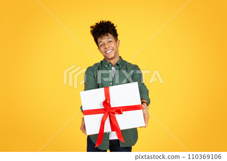 Happy handsome young black guy giving present, yellow background 110369106