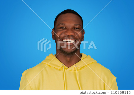 An African man in a yellow hoodie beams with a radiant smile, showcasing white teeth An African man in a yellow hoodie beams with a radiant smile, showcasing white teeth 110369115
