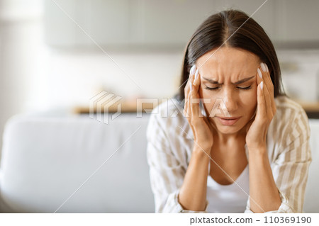 Woman in distress with severe headache, pressing her temples and frowning 110369190