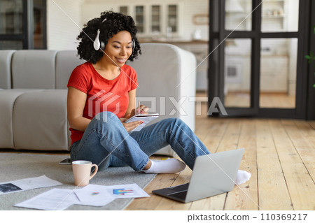 Focused young black woman writing in notepad while and using a laptop 110369217