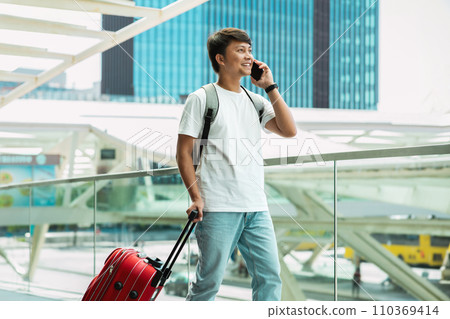 Asian guy tourist walking by airport, talking on phone Asian guy tourist walking by airport, talking on phone 110369414