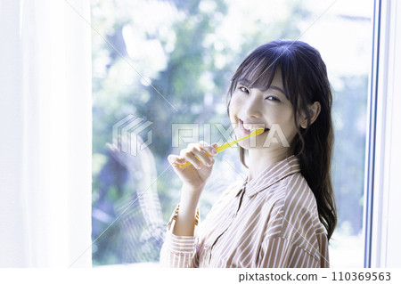 Young woman in pajamas brushing her teeth Young woman in pajamas brushing her teeth 110369563