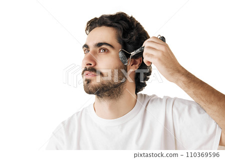 Close up portrait of man moves smoothly over skin of his face with massage roller against white studio background. Concept of facial care routine. 110369596