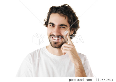 Portrait of brunette young man with perfect soft skin applies facial cream on face skin against white studio background. 110369604