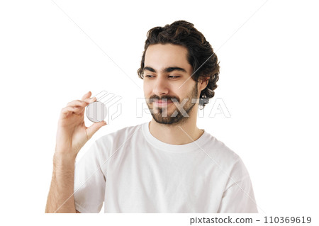 Brunette, handsome young man with beard holding jar of cosmetic product in hand. Male model looks well-groomed and healthy. Brunette, handsome young man with beard holding jar of cosmetic product in hand. Male model looks well-groomed and healthy. 110369619