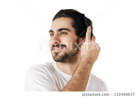 Young attractive brunette man with beard brushing his long and curly hair against white studio background. Concept of hair care, hygiene. 110369637
