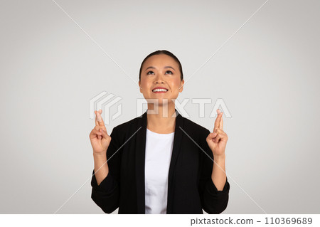 Happy young asian woman in suit crossed fingers, looking up at empty space Happy young asian woman in suit crossed fingers, looking up at empty space 110369689