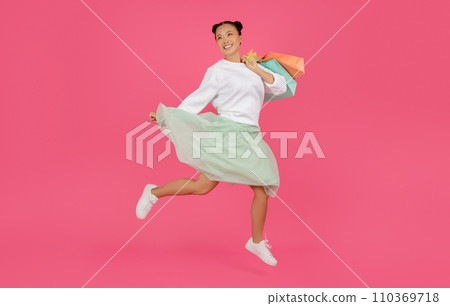 Happy asian woman jumping high with shopping bags in her hands Happy asian woman jumping high with shopping bags in her hands 110369718