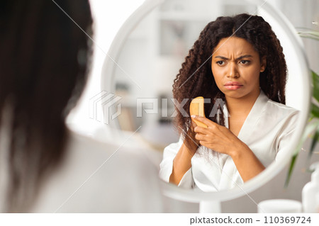 Upset Black Lady Combing Hair With Bamboo Brush Near Mirror At Home 110369724