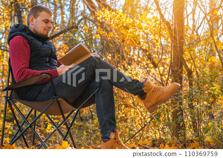 Young man is sitting on chair in an autumn park or Young man is sitting on chair in an autumn park or 110369759