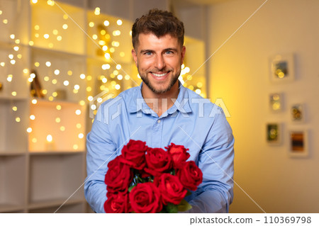 Smiling man with bouquet of red roses, festive background lights Smiling man with bouquet of red roses, festive background lights 110369798