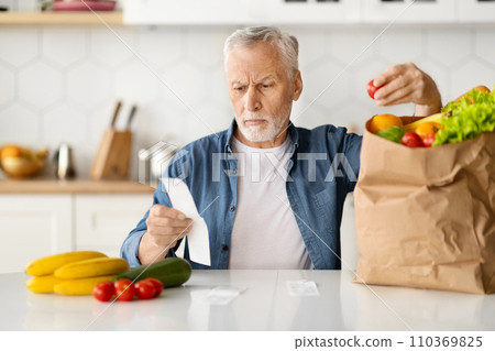 Serious senior man checking bill and examining groceries after food shopping 110369825