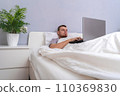 A man with laptop is lying in bed. Freelancer 110369830