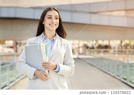 A contented young woman secretary, manager in a smart suit holds files, walking with confidence 110370022
