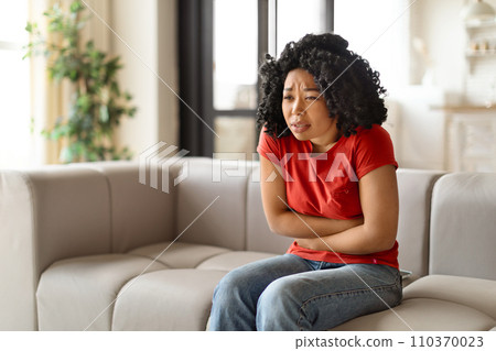 Worried young black woman sitting arms crossed and looking troubled 110370023