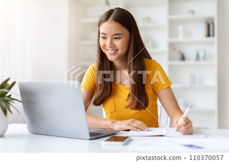 Online Lesson. Smiling Young Asian Woman Using Laptop And Taking Notes 110370057