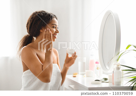 Attractive Young African American Woman Applying Nourishing Cream On Face 110370059