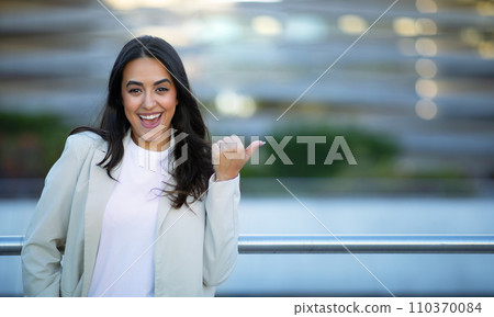 Cheerful Arabic Businesswoman Pointing Thumb Aside At Copy Space Outdoors Cheerful Arabic Businesswoman Pointing Thumb Aside At Copy Space Outdoors 110370084
