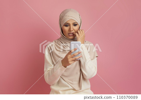 Shocked arab muslim woman in hijab looking at smartphone and biting nails 110370089