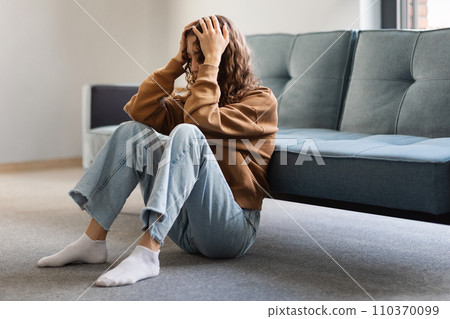 Young teen lady alone sitting depressed touching head at home Young teen lady alone sitting depressed touching head at home 110370099