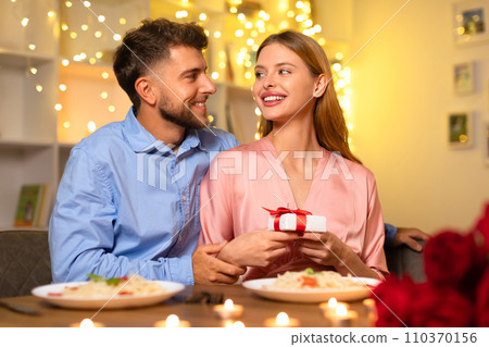 Man gazing at woman with gift, romantic dinner backdrop Man gazing at woman with gift, romantic dinner backdrop 110370156