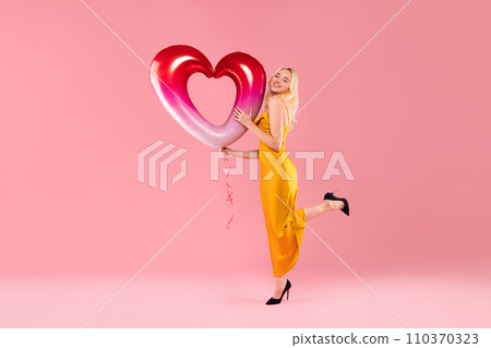 Playful woman lifting heart balloon on tiptoe 110370323
