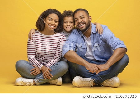 Happy african american family of three sitting on floor and embracing 110370329