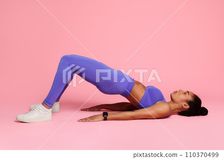 Young black woman in activewear practicing yoga bridge pose, studio 110370499