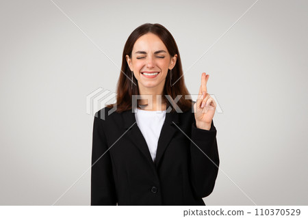 Cheerful young European woman in suit crossed her fingers and make a wish sign 110370529