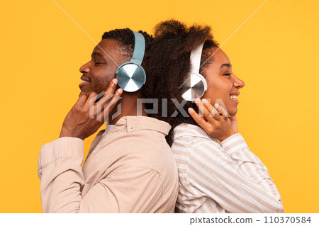 Side view of black couple with headphones back-to-back, enjoying music 110370584