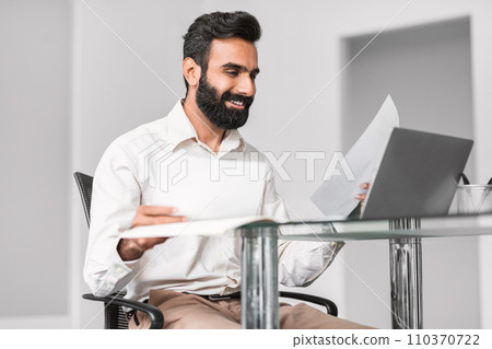 Cheerful indian professional reading documents with a smile Cheerful indian professional reading documents with a smile 110370722