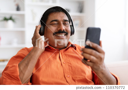 Closeup positive mature indian man using headphones, smartphone 110370772