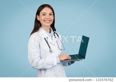 Smiling woman doctor using laptop on light blue background 110370782