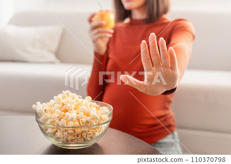 Unrecognizable Pregnant Woman Refusing Unhealthy Popcorn Choosing Apple Indoor, Cropped 110370798